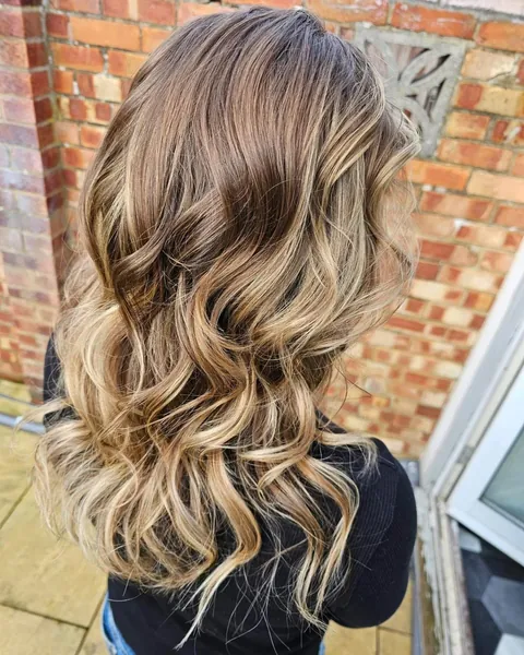 Long balayage with brunette roots melting into soft golden blonde waves