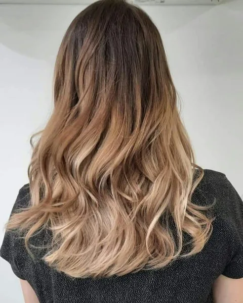 Long brunette hair blending into a soft caramel ombré, styled in loose waves